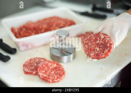 Hamburger di manzo crudo in mano al macellaio Foto Stock