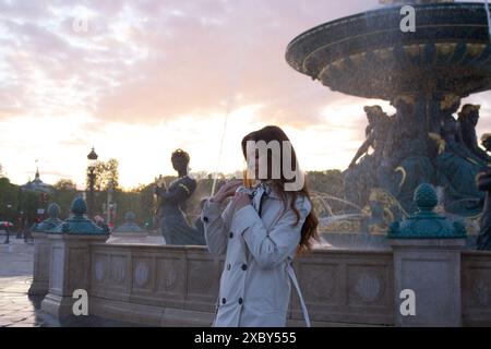 Una bella ragazza sta accanto a una fontana al tramonto su una piazza di Parigi in primavera Foto Stock