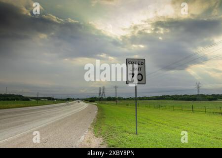 Texas Highway: Un cartello con il limite di velocità "70" si erge sullo sfondo di cieli spettacolari e vegetazione lussureggiante, mentre le nuvole di tempesta primaverile lasciano il posto a una luce vibrante. Foto Stock