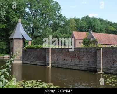 Una torre in mattoni e un muro sul bordo dell'acqua con gigli sullo stagno, circondati da alberi, giardini e fiori al sole brillante, ochtrup Foto Stock