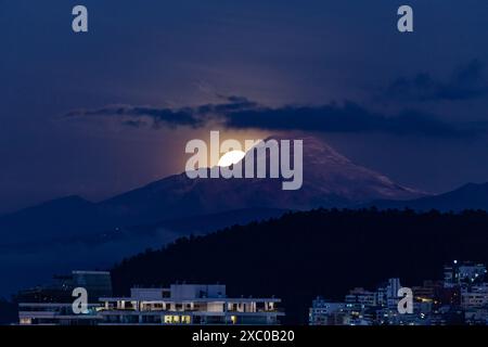 La luna aparece poco a poco muy brillante atras del volcan Cayambe en Quito Foto Stock