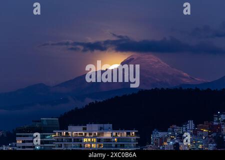 La luna aparece poco a poco muy brillante atras del volcan Cayambe en Quito Foto Stock