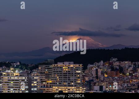 Resplandor de luz de la luna saliendo atrás del Volcán Cayambe al anochecer Foto Stock