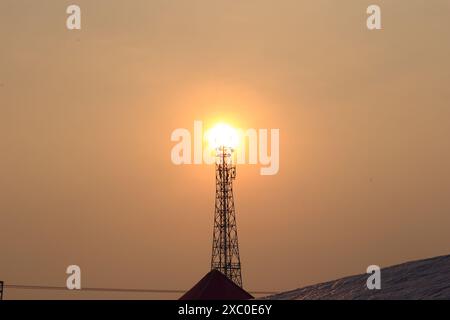 Una torre di telefoni cellulari solitaria si erge in alto sullo sfondo del sole che tramonta. Foto Stock