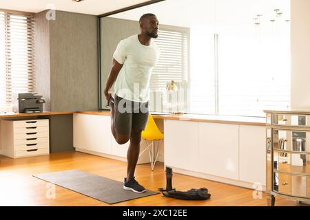 Adatta un uomo afroamericano che lavora, si allunga e si allena in una casa moderna con pavimenti in legno Foto Stock
