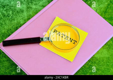 Concetto di copyright. Scrittura DI BREVETTI attraverso una lente d'ingrandimento su un adesivo giallo posizionato su un notebook aziendale su uno sfondo verde Foto Stock