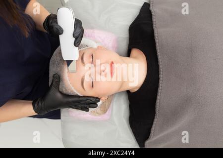 Peeling del viso a ultrasuoni. Giovane donna che ottiene pelle di buccia ultrasonica con scrubber della pelle alla clinica di cosmetology. Foto Stock