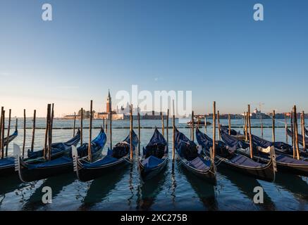 Gondole coperte attraccate con Chiesa sullo sfondo a Venezia, Italia. Foto Stock