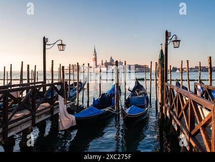 Gondole coperte attraccate con Chiesa sullo sfondo a Venezia, Italia. Foto Stock