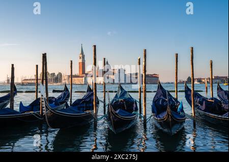 Gondole coperte attraccate con Chiesa sullo sfondo a Venezia, Italia. Foto Stock