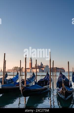 Gondole coperte attraccate con Chiesa sullo sfondo a Venezia, Italia. Foto Stock