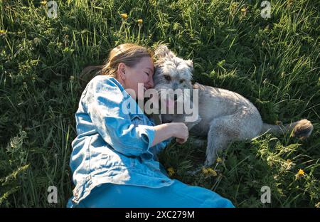 la giovane donna con un cane senza razza è sdraiata sull'erba Foto Stock