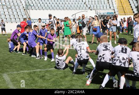 ODESSA, UCRAINA, 9 giugno 2024: Squadre per bambini giocano a tiro di guerra al festival sportivo. Lotta di squadra sportiva - tiro alla fune sull'erba verde del prato dello stadio. Chi Foto Stock