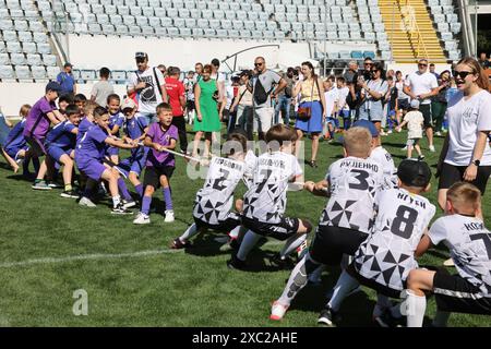 ODESSA, UCRAINA, 9 giugno 2024: Squadre per bambini giocano a tiro di guerra al festival sportivo. Lotta di squadra sportiva - tiro alla fune sull'erba verde del prato dello stadio. Chi Foto Stock