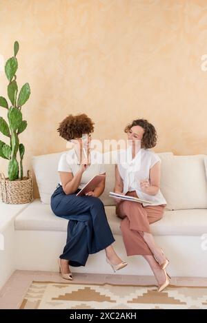 Due donne d'affari sedute sul divano che ridono Foto Stock