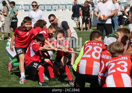 ODESSA, UCRAINA, 9 giugno 2024: Squadre per bambini giocano a tiro di guerra al festival sportivo. Lotta di squadra sportiva - tiro alla fune sull'erba verde del prato dello stadio. Chi Foto Stock