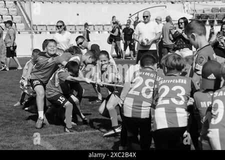 ODESSA, UCRAINA, 9 giugno 2024: Squadre per bambini giocano a tiro di guerra al festival sportivo. Lotta di squadra sportiva - tiro alla fune sull'erba verde del prato dello stadio. Chi Foto Stock