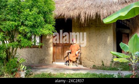Nha Trang, provincia di Khanh Hoa, Vietnam - 9 giugno 2024: Una donna siede davanti al fango - murata di una casa di paglia a Nha Trang, provincia di Khanh Hoa, Vietnam Foto Stock