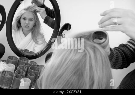 Mamma che arriccia i capelli di una ragazzina caucasica che si guarda allo specchio, USA. Foto Stock