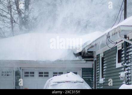 Guardando la neve che soffia dal tetto di una casa residenziale durante una bufera di vento forte. Foto Stock