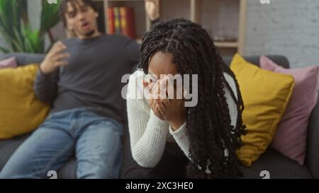 Una donna in difficoltà copre il suo viso con le mani accanto a un uomo frustrato su un divano, raffigurando la discussione di una coppia in un salotto. Foto Stock