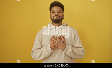 Uomo di colore adulto con le mani sul petto, con cappuccio, si staglia su sfondo giallo e sembra contento. Foto Stock