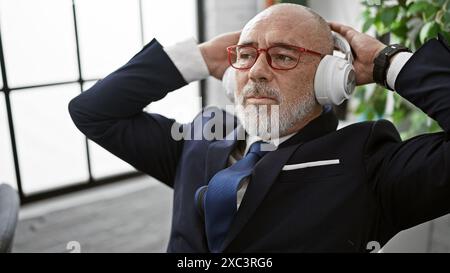 Un uomo di mezza età in costume ama la musica con le cuffie in un ufficio moderno. Foto Stock
