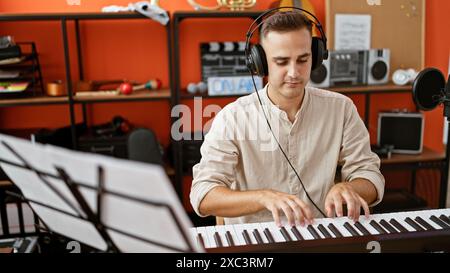 Un giovane concentrato suona la tastiera in uno studio musicale con cuffie, microfoni e apparecchiature audio intorno a lui. Foto Stock