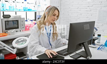 Una giovane donna caucasica concentrata che lavora diligentemente in un laboratorio ben attrezzato, circondato da attrezzature scientifiche. Foto Stock