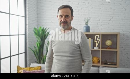 Un uomo dalla barba matura si trova in un elegante salotto, in un ambiente interno che trasuda eleganza e calore casual. Foto Stock