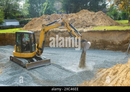 Nei cantieri edili, un escavatore riempie le irregolarità degli scavi con la base di macerie di granito, che verrà utilizzata per le fondamenta in calcestruzzo Foto Stock