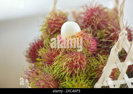 Rambutan fresco e maturo, dolce frutto tropicale pelato con foglie, frutti Rambutan su cesto raccolta di fondo dall'albero rambutan del giardino. Foto Stock