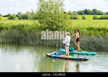 Due giovani donne in paddleboard sul fiume Tamigi a Kelmscott, Oxfordshire, Inghilterra Regno Unito Foto Stock