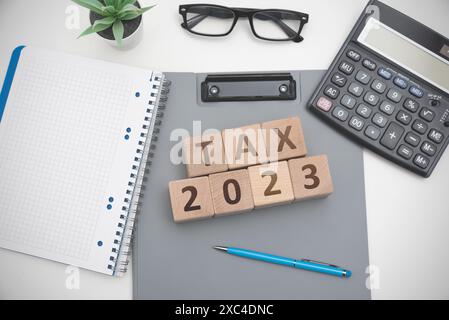 Un blocco di legno con la parola "tassa 2023" è sopra una pila di carte Foto Stock