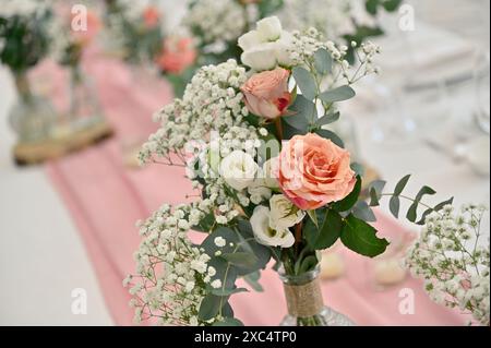 Un elegante centrotavola con rose di pesca e fiori bianchi, ideale per matrimoni e occasioni speciali, adagiato su un tovagliolo rosa. Foto Stock