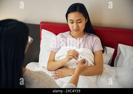 Donna malata che riceve un dispositivo di misurazione della temperatura dalla madre premurosa Foto Stock