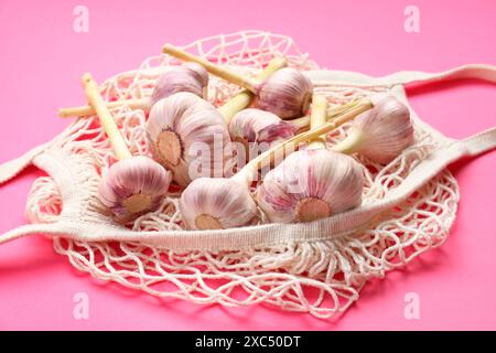 Borsa a cordoncino con teste d'aglio su sfondo rosa brillante, primo piano Foto Stock