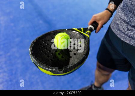 Uomo che tiene una racchetta di padel in un campo blu con una palla gialla Foto Stock