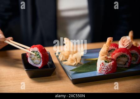 Primo piano donna che immerge il rotolo di tobiko nella salsa di soia Foto Stock