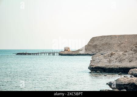 Minimalista e tranquillo sfondo di viaggio con una piccola casa solitaria e il molo in rovina. Costa sabbiosa e rocciosa in Egitto. Spiaggia desolata sulla costa di Foto Stock