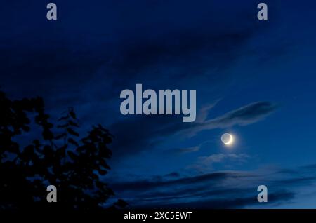 Luna nuova nel cielo blu con piccole nuvole Foto Stock