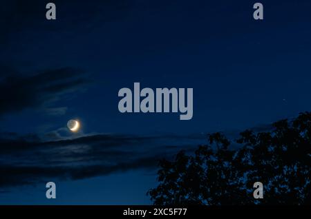 Luna nuova nel cielo blu con piccole nuvole Foto Stock