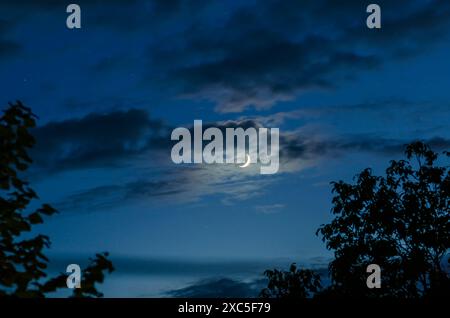 Luna nuova nel cielo blu con piccole nuvole Foto Stock