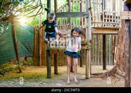 i bambini giocano all'aperto nella palestra della giungla di legno, saltando dalla piattaforma Foto Stock