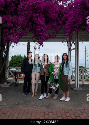 Lima, Perù - luglio 30 2023: La famiglia posa guardando la macchina fotografica in un parco con Bougainvillea sul tetto che si affaccia sul mare in un giorno nuvoloso Foto Stock