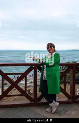 Lima, Perù - luglio 30 2023: Donna peruviana che indossa un cappotto verde si appoggia su un balcone rosso e guarda la fotocamera Foto Stock