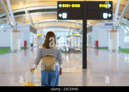 Vista posteriore di una donna asiatica che attraversa un moderno e spazioso terminal aeroportuale Foto Stock