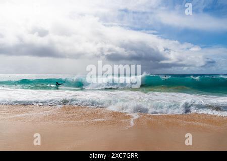 Una persona è in piedi su una splendida spiaggia, guardando le ipnotiche onde dell'oceano sotto un vasto cielo pieno di nuvole soffici Foto Stock
