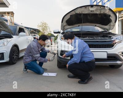 Due persone ispezionano i danni su un veicolo. Il proprietario dell'auto indica un'ammaccatura sul paraurti dell'auto. Uno staff assicurativo che scatta foto con lo smartphone Foto Stock