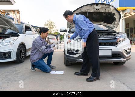 Due persone ispezionano i danni su un veicolo. Il proprietario dell'auto indica un'ammaccatura sul paraurti dell'auto. Uno staff assicurativo che scatta foto con lo smartphone Foto Stock